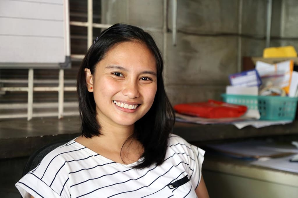 A woman wearing a striped nursing uniform, smiles at the camera.